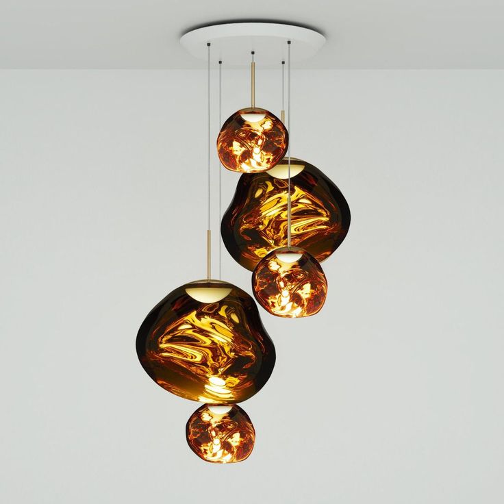 The Melt Mini Round Pendant System (Copy) features five amber glass globes in different sizes, each suspended by black cords from the ceiling, set against a plain white background.